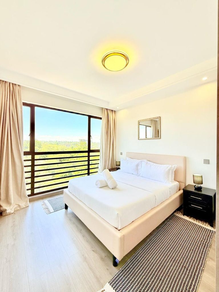 well lit bedroom with view of trees from the large windows at the Fully Furnished 3 bedroom Apartment in Westlands