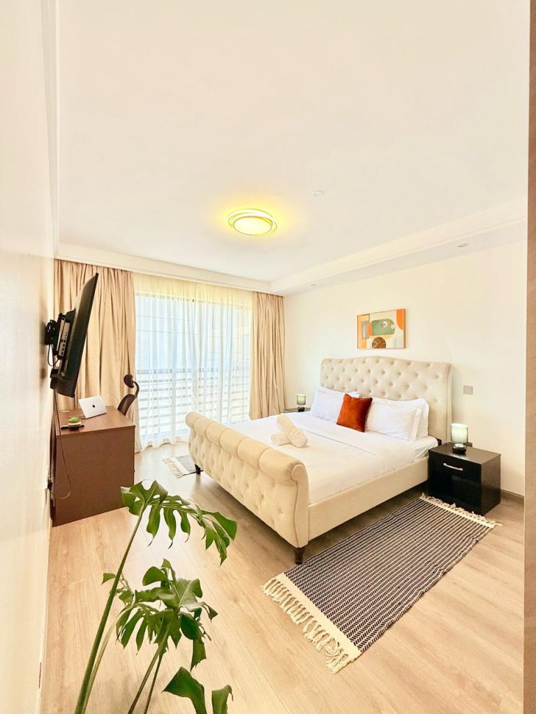 a bedroom with a king size bed, large windows with curtains, a mounted smart tv and white linens at the Fully Furnished 3 bedroom Apartment in Westlands