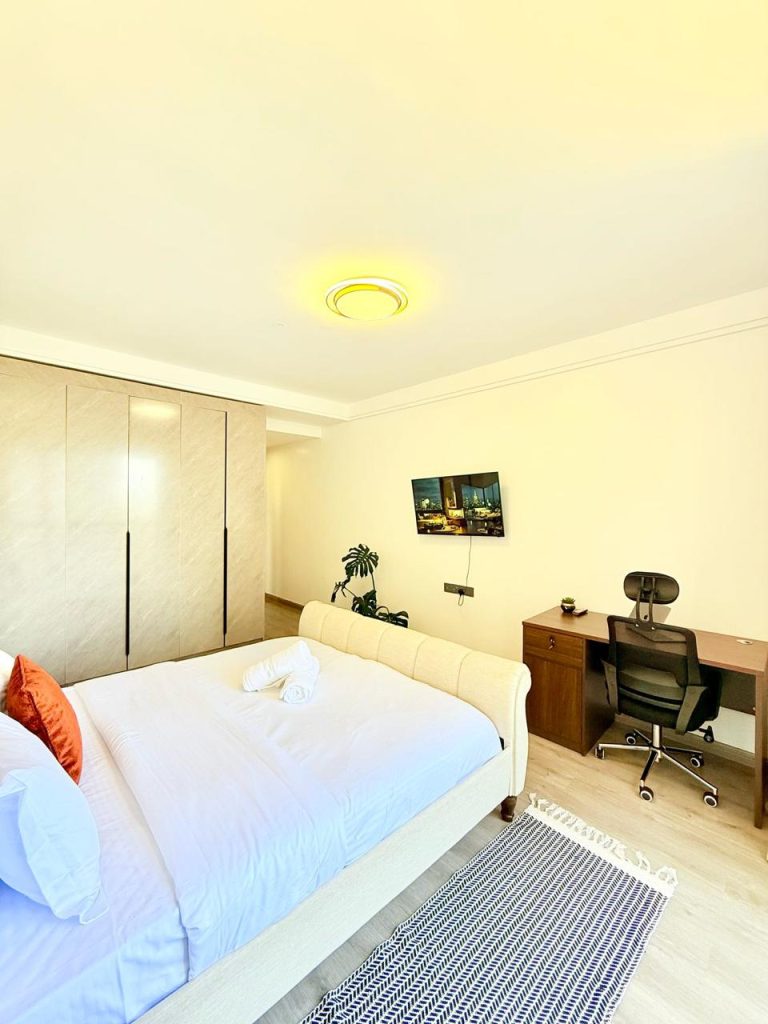 bedroom view of the inbuilt wardrobes, study desk, mounted smart tv and partial part of the bed at the Fully Furnished 3 bedroom Apartment in Westlands
