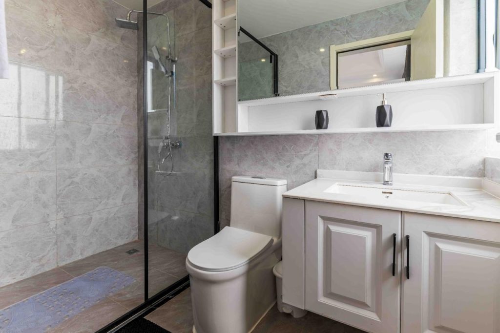 classic bathroom with cubicle glass shower, a toilet and sink with storage cabinets and a large mirror