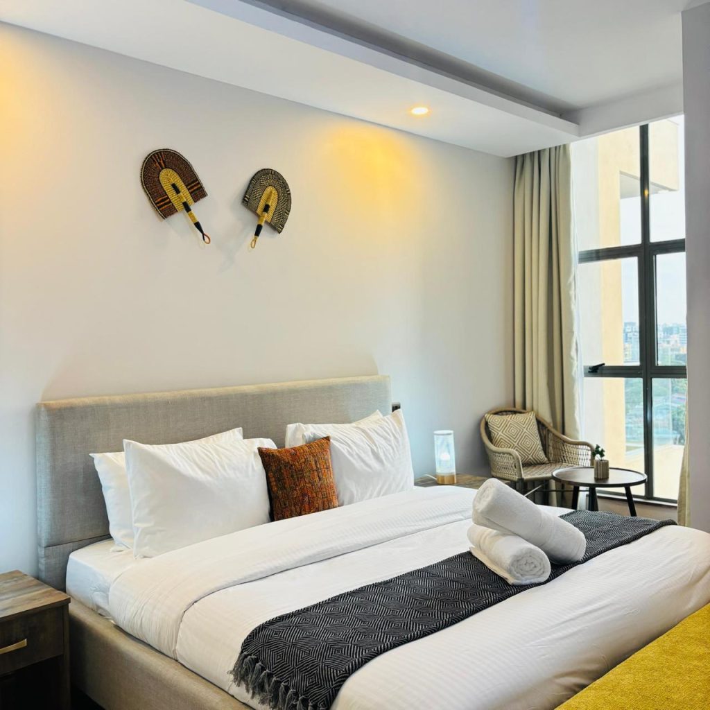 a bedroom with an accent chair with a table, king size bed with white beddings and partial view of the large windows at Furnished 3 bedroom Apartment in Gated Community