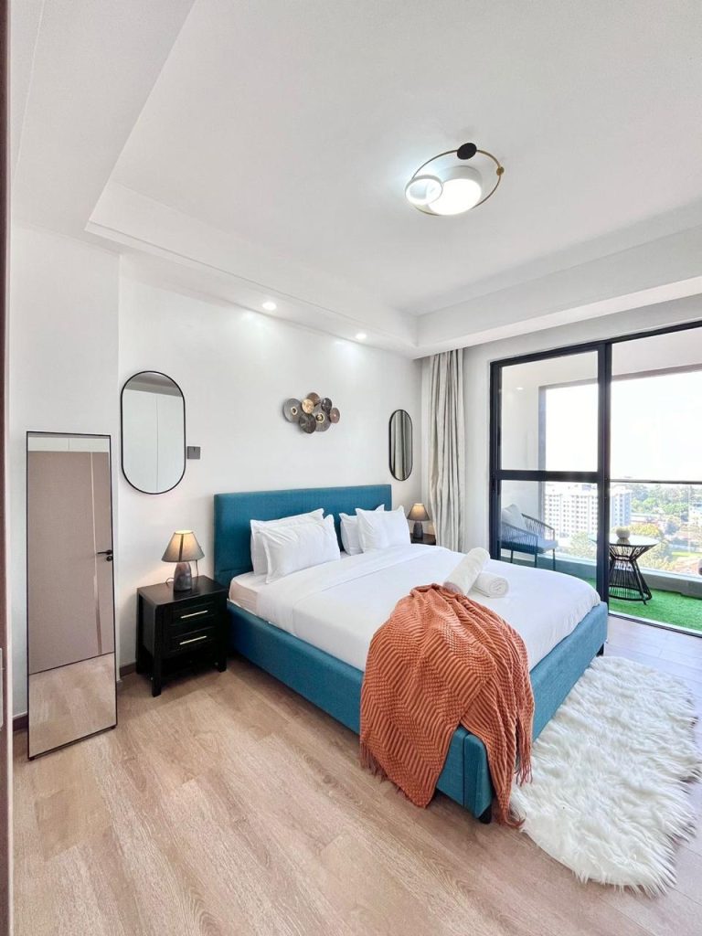 bedroom with a full length mirror, a king size bed and large sliding windows opening to a balcony at Two Bedroom Furnished Apartment for rent in Nairobi