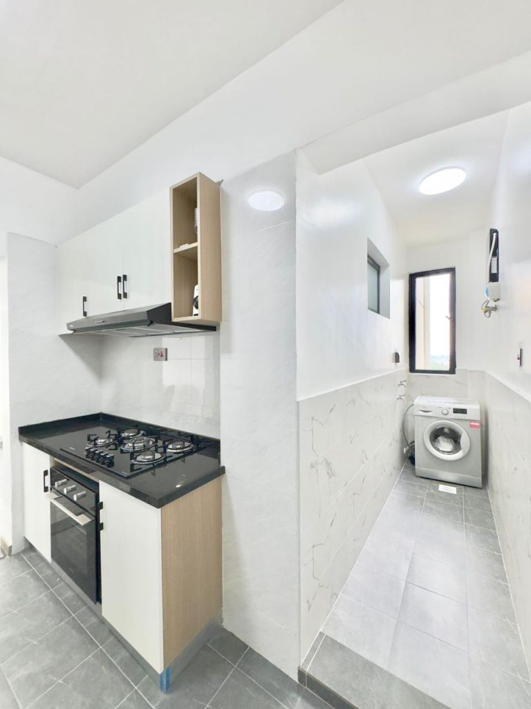 the laundry area fitted with a washing machine and the partial view of the kitchen cooker and hood at the furnished Two Bedroom Furnished Apartment for rent in Nairobi