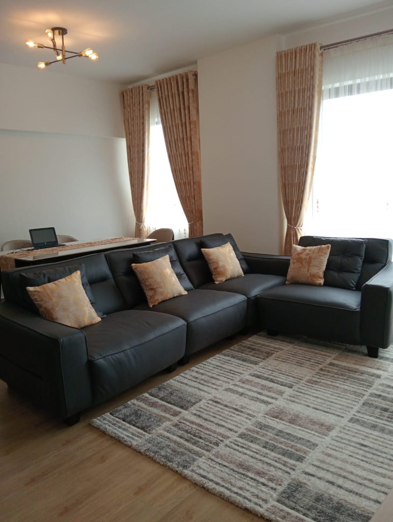 a large couch with the view of the large windows covered in white sheers at Furnished 2-Bedroom Apartment for Daily Rentals in Kilimani
