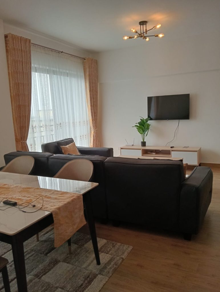 mounted tv in the living room with a couch and aprtila view of the dining set at the Furnished 2-Bedroom Apartment for Daily Rentals in Kilimani