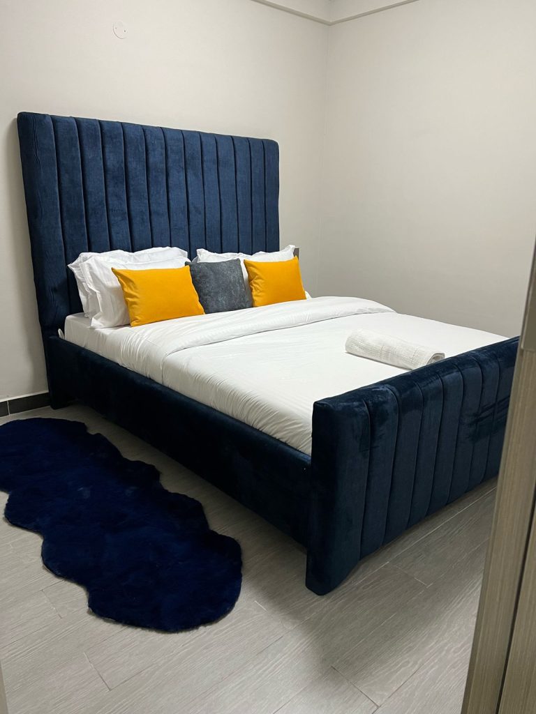 soft blue headboard bed with white linen and yellow and grey throw pillows at Furnished 2 bedroom Apartment Ideal for Extended Stay