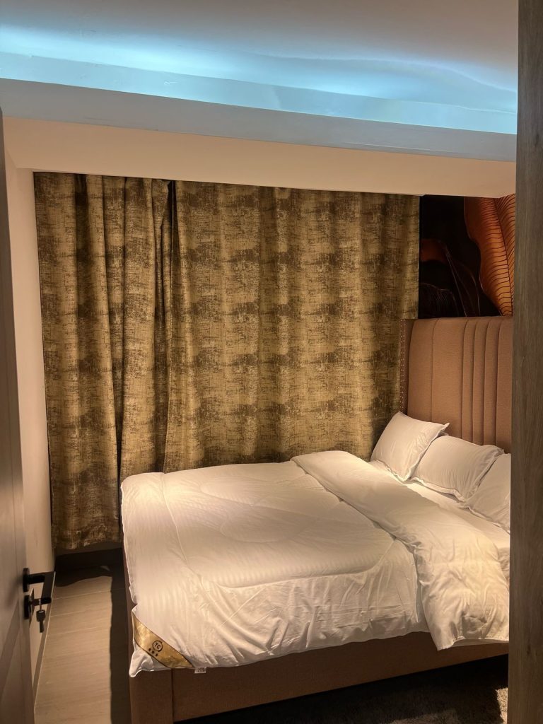 bedroom with a king size bed, white linen and large windows covered by a curtain at Furnished Apartment with Rooftop Terrace in Kilimani