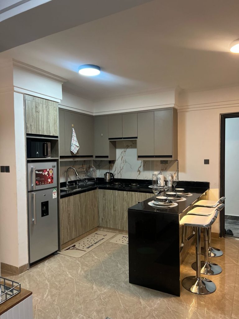 An open plan kitchen with a breakfast bar , fitted cabinets and appliances at Furnished Apartment with Rooftop Terrace in Kilimani