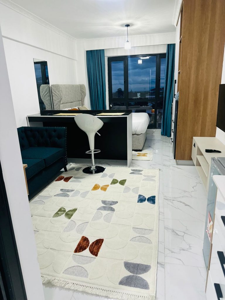 the view of the large windows , a bed, a breakfast bar, a couch and partial view of the Tv and fridge at Furnished Studio Airbnb in Kilimani Nairobi