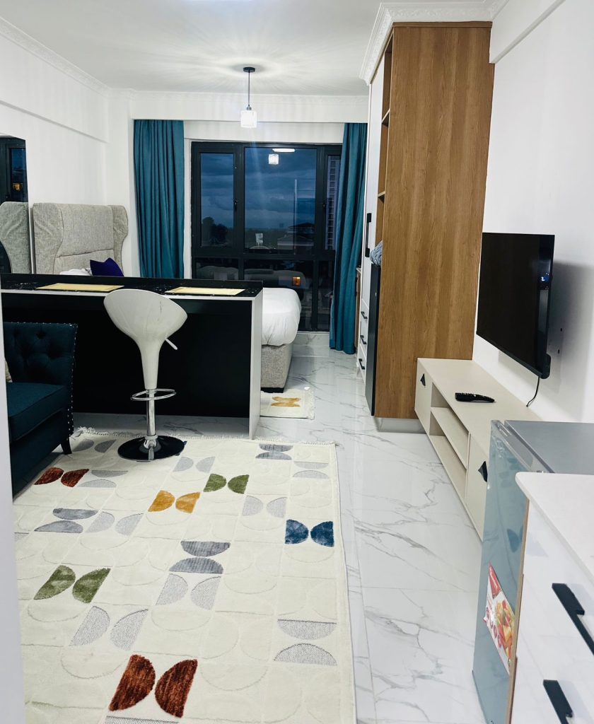 view of the kitchen island. a mounted smart Tv, inbuilt wardrobes and a couch at the Furnished Studio Airbnb in Kilimani Nairobi
