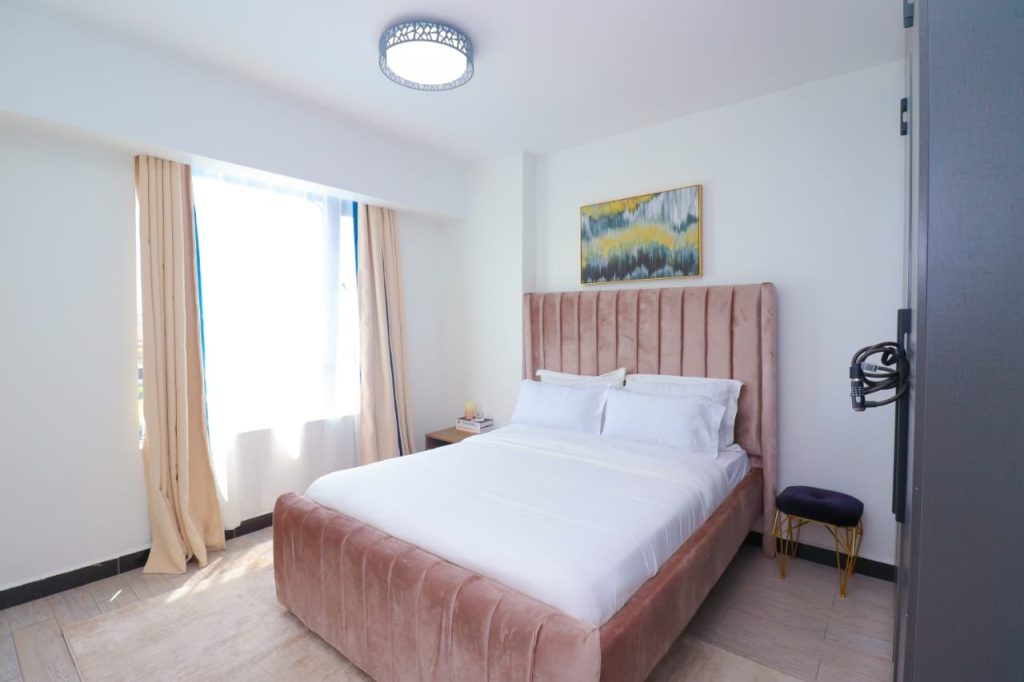 a queen size bed with white linens and large windows with curtains at Furnished 3 Bedroom Airbnb in Kilimani