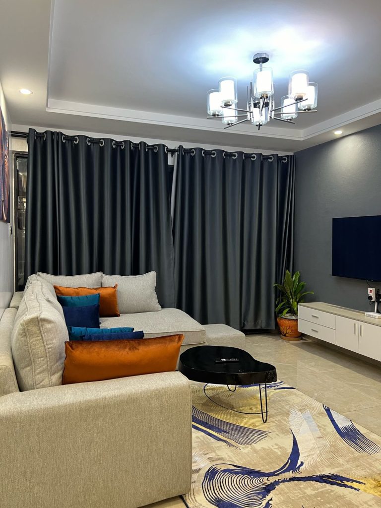 The view of the couch and curtains and the partial view of the mounted smart Tv at Airbnb-style Furnished Apartment in Lavington