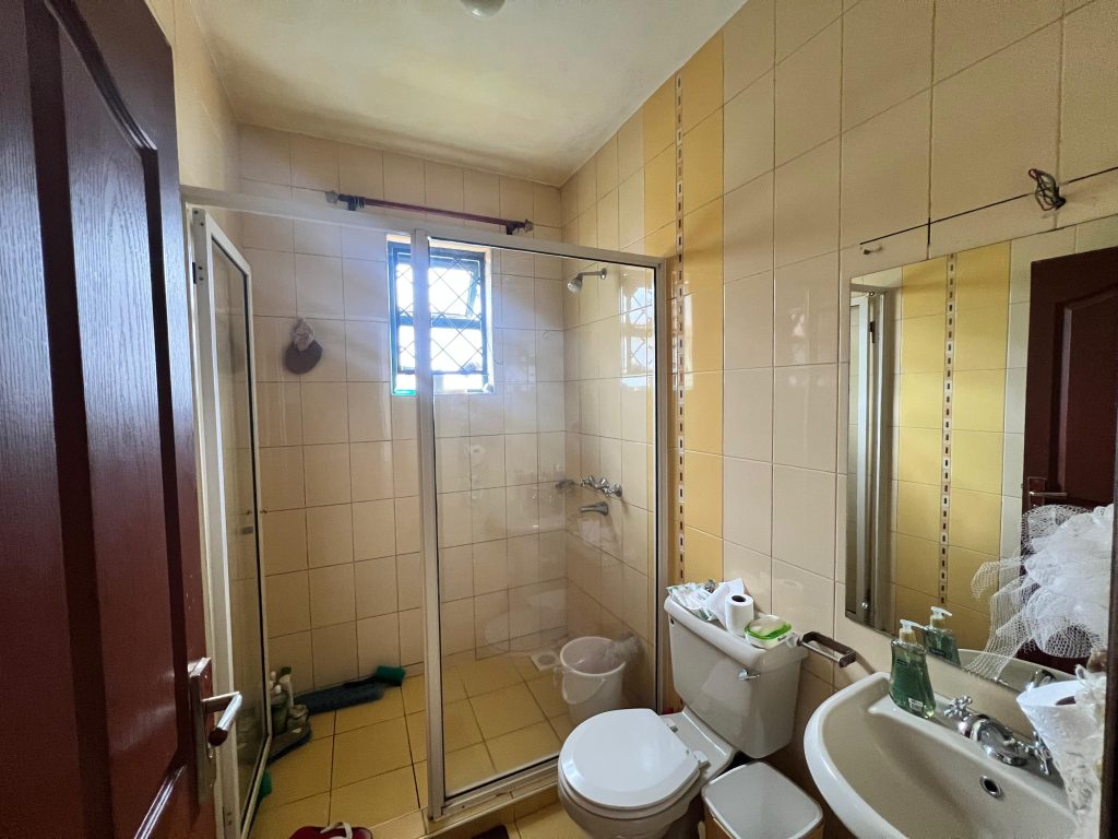 bathroom with cubicle glass shower, a toilet and a sink with a mirror at White Oak Park Apartments in Kilimani