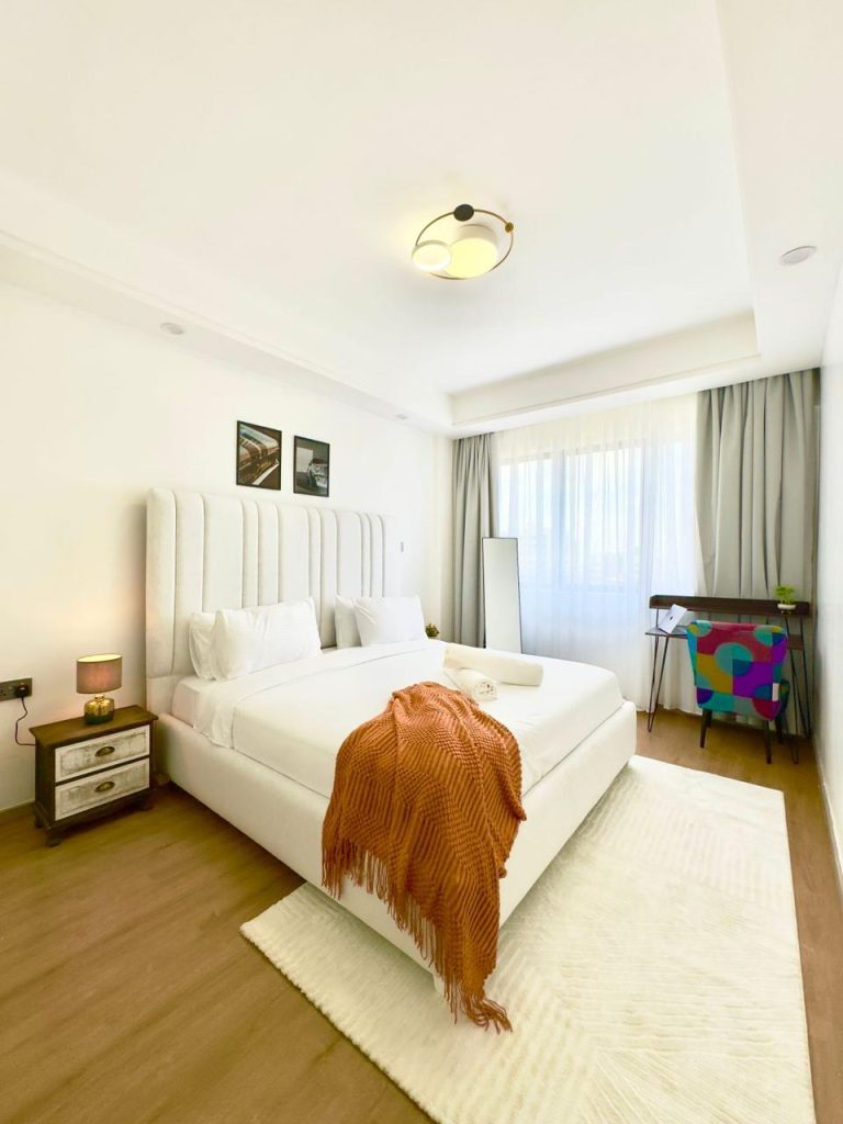 a bedroom with a king size bed with white beddings, a study desk and a mirror at Business accommodation near Yaya Centre Kilimani