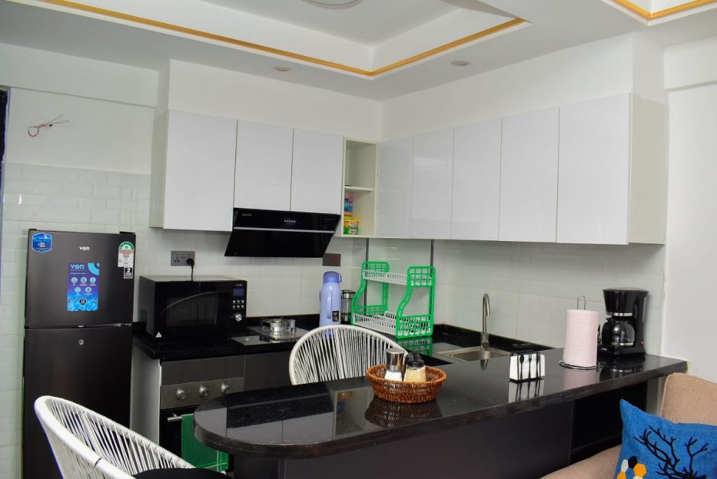 Fully equipped open plan kitchen with cooker, microwave, extractor hood, and upper and lower cabinets in an affordable furnished apartment in Kileleshwa Nairobi.