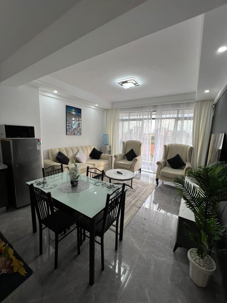 Bright living room of 1 Bedroom Furnished Apartment in Kileleshwa with dining area, fridge, two single-seater couches, and a three-seater sofa.