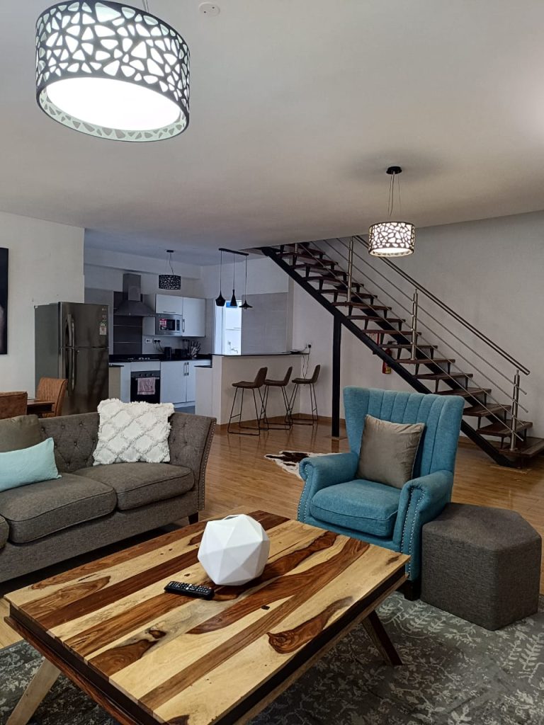 Serviced 2 Bedroom Duplex Apartment in Nairobi with 2-seater and single-seater sofa, staircase and open plan layout in view