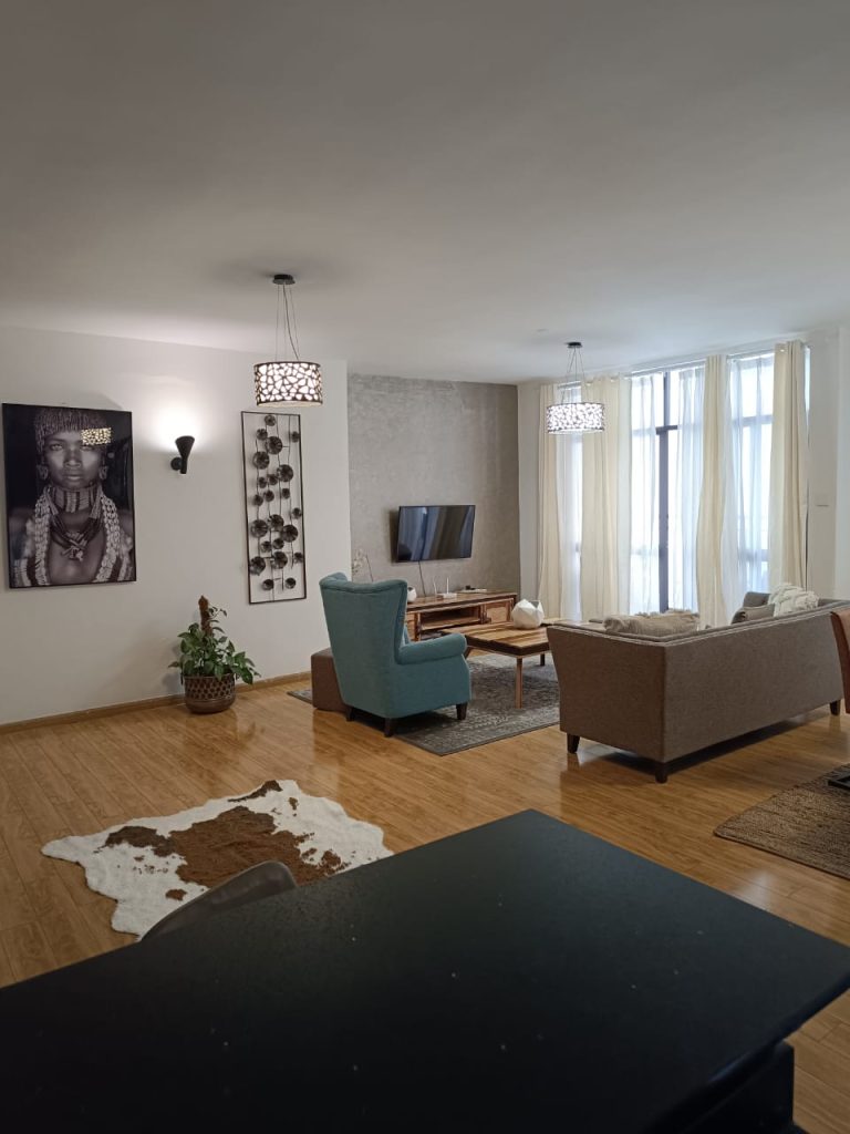 Spacious living area with elegant sofas, large windows, and chandelier – Serviced 2 Bedroom Duplex Apartment in Nairobi