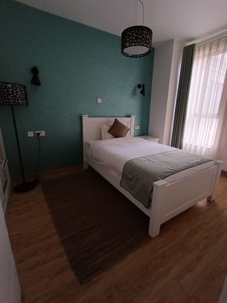 Third bedroom with a cozy bed and natural lighting from large windows in a Kilimani furnished duplex apartment