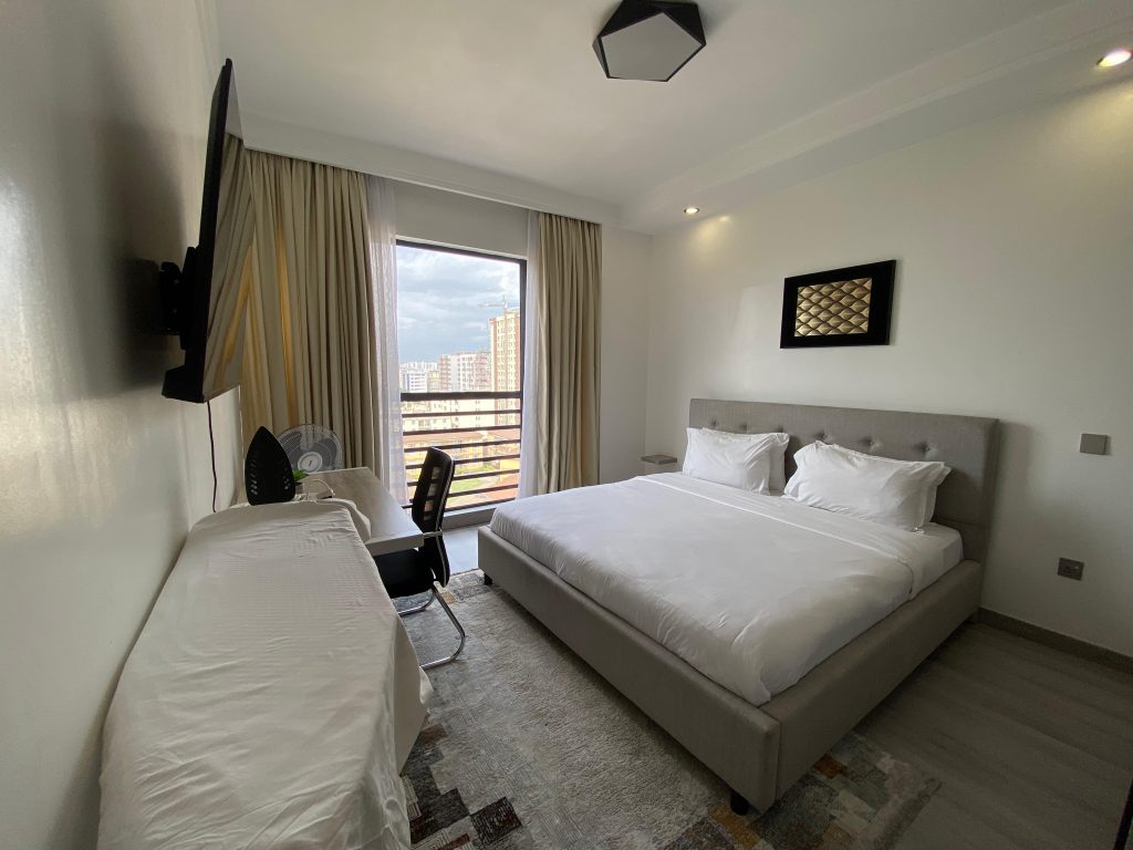 Master ensuite bedroom with king size bed, mounted smart TV, and large windows in a fully furnished 2 bedroom unit.
