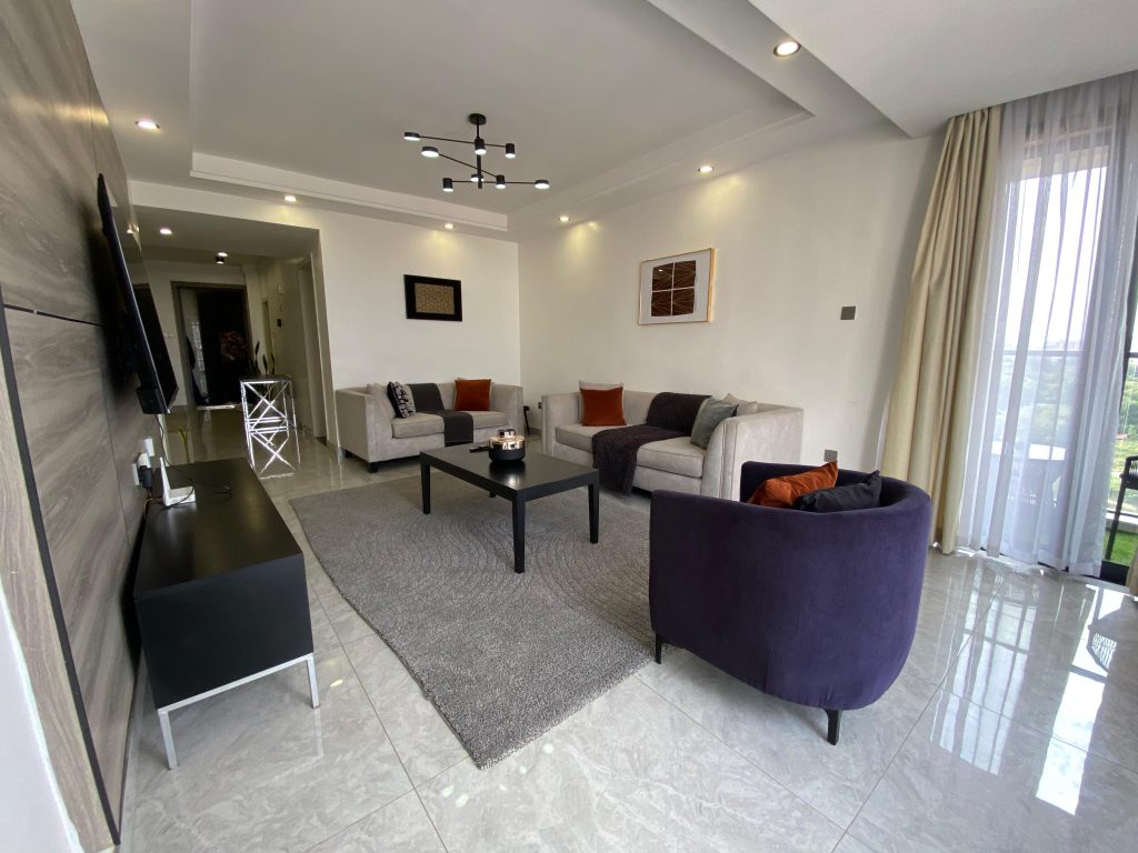 Spacious lounge in a fully furnished 2 bedroom master ensuite with cozy sofas, large windows, and a chandelier.