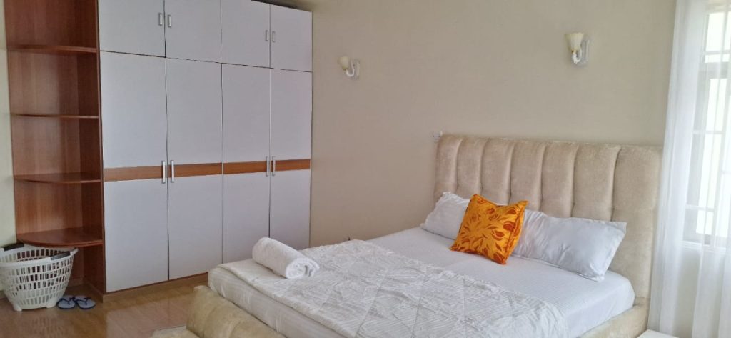 Partial view of bedroom showing white bed and built-in wardrobes – Luxury 3 Bedroom Serviced Apartment in Nairobi