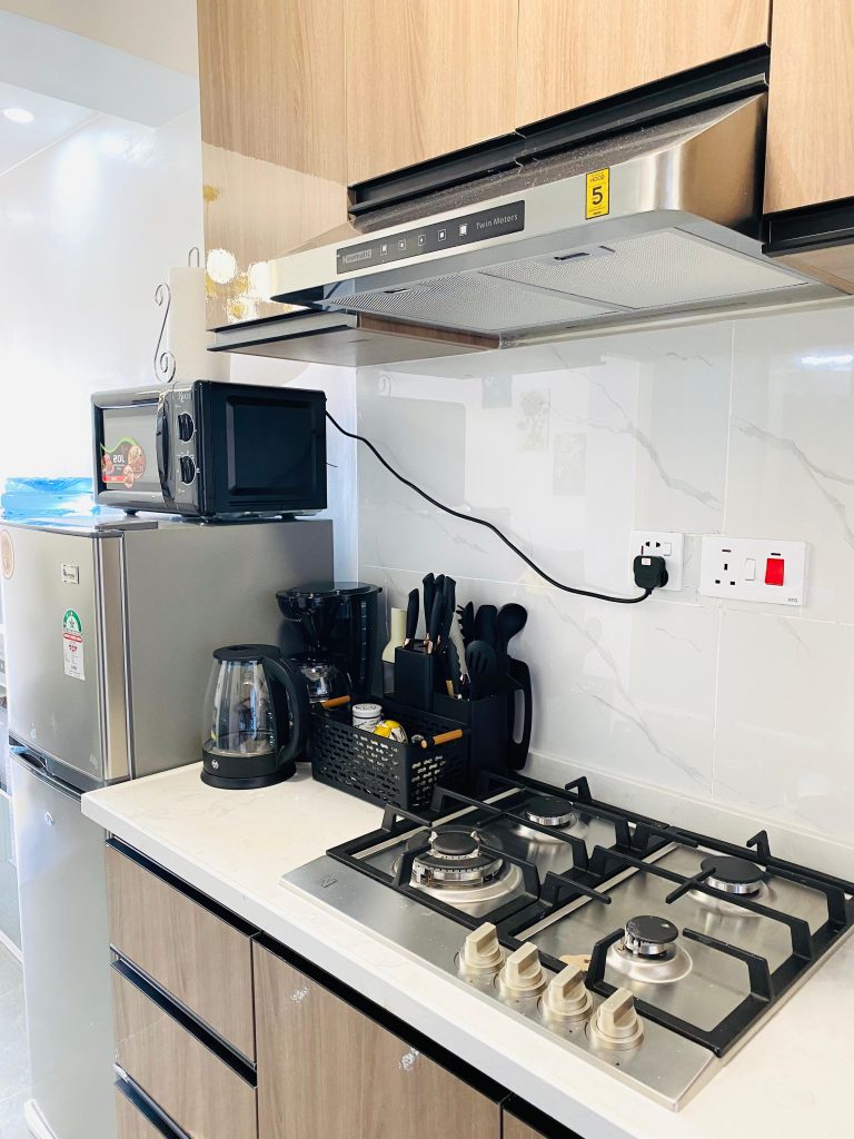 Fully equipped kitchen with cooker hood, coffee maker, fridge, and microwave in an affordable 1-bedroom furnished apartment in Nairobi.