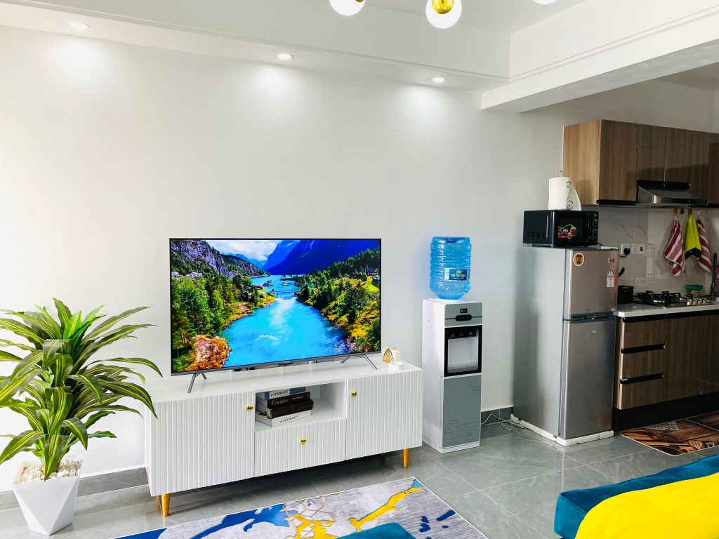 Smart TV setup with water dispenser and fridge inside an affordable 1-bedroom furnished apartment in Nairobi.