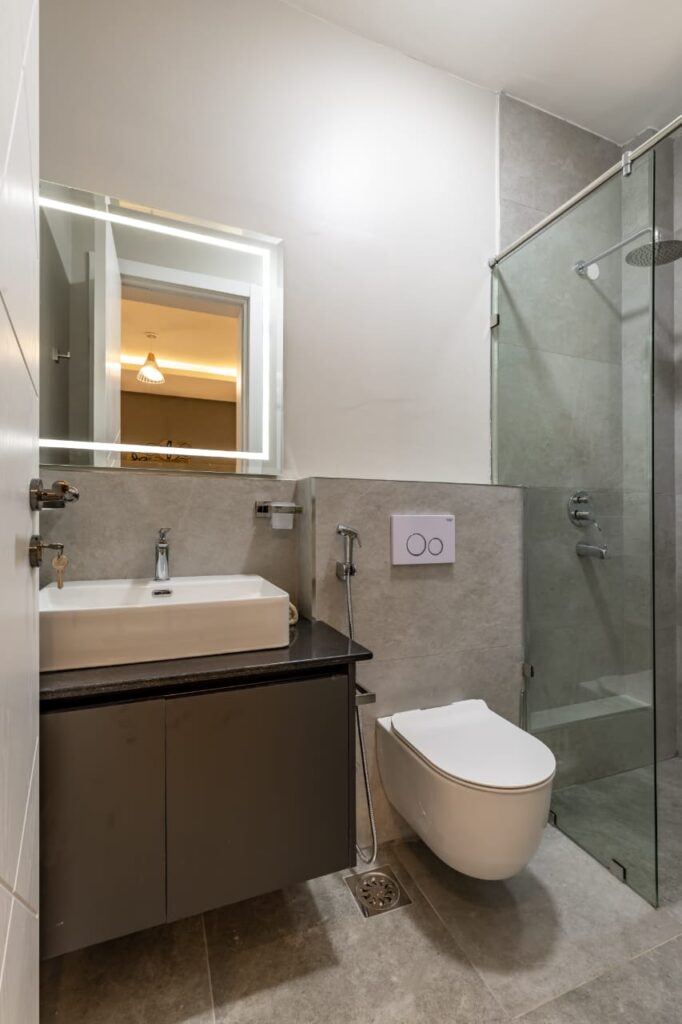 a bathroom with glass cubicle shower, a toilet and a sink with a mirror and storage space at the 3 bedroom apartment along General Mathenge Gardens
