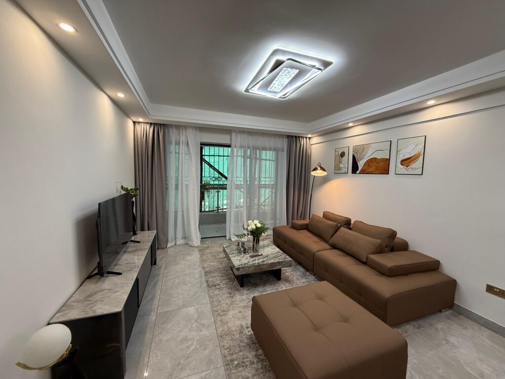 A bright living room with a Smart Tv,a coffee table, a couch and large windows at the Two Bedroom Apartment Near Nyeri Road